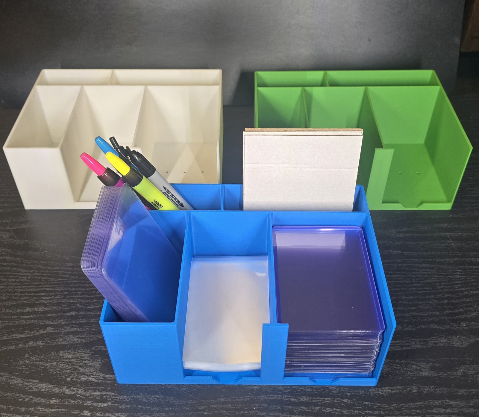 Three Card Packing Station Organizers together in blue, white, and green, with the blue one loaded with toploaders, sharpies, and cards
