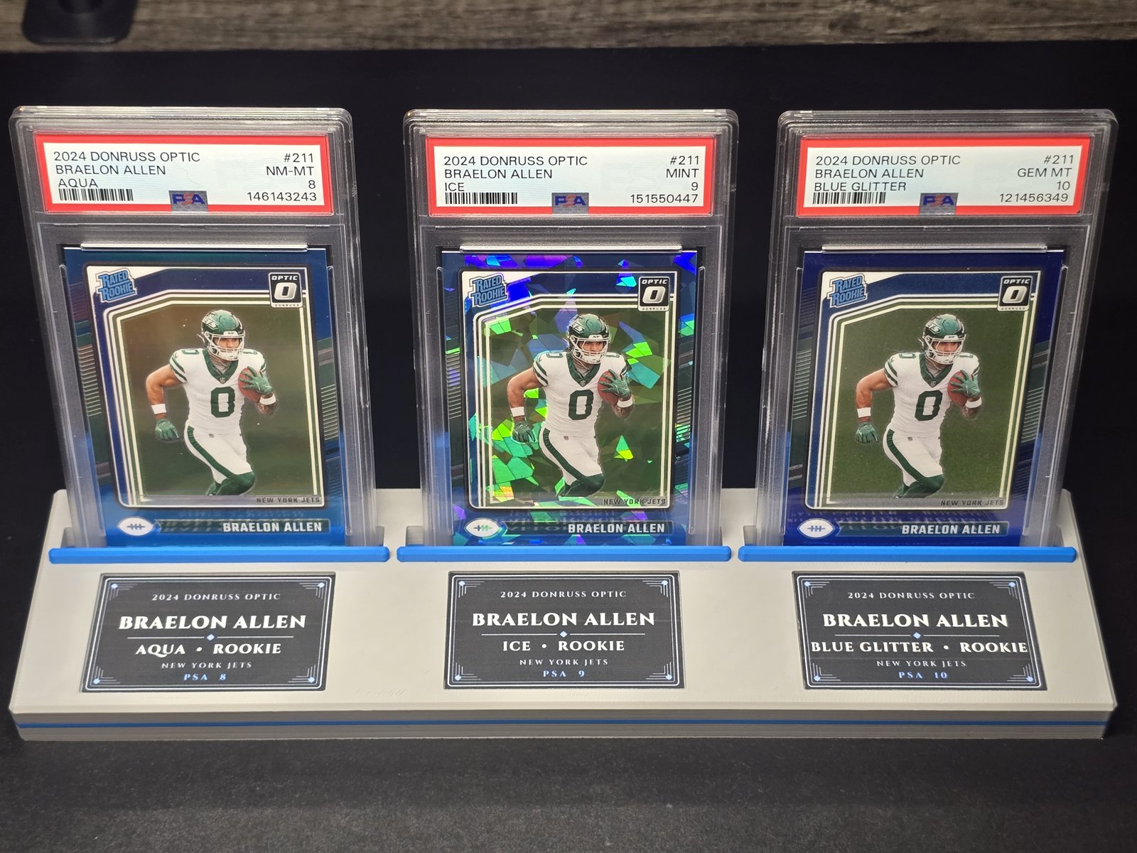 The stand holding three PSA slabs with personalized name plates beneath each card